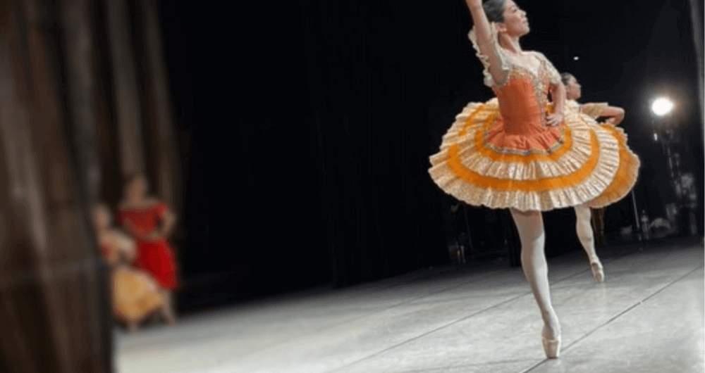 舞台上でオレンジの衣装で踊るバレリーナ。